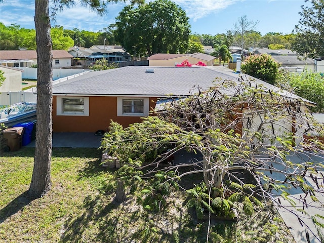 rear view of property featuring a shingled roof, fence, a residential view, stucco siding, and a yard