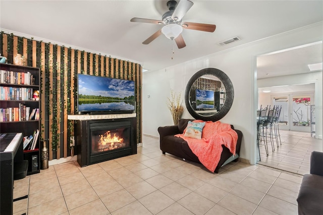 living area featuring visible vents, ornamental molding, a ceiling fan, a large fireplace, and tile patterned flooring