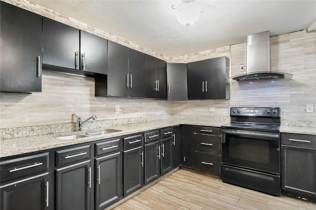 kitchen with dark cabinetry, electric range, a sink, wall chimney range hood, and tasteful backsplash