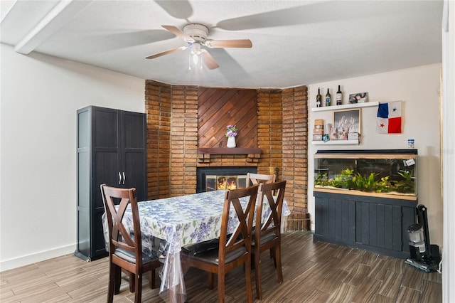 dining room with baseboards, a ceiling fan, a brick fireplace, and wood tiled floor