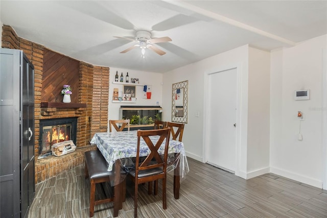 dining area with baseboards, wood tiled floor, ceiling fan, and a fireplace