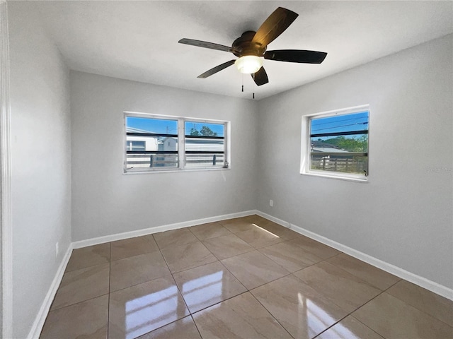 tiled empty room with baseboards and a ceiling fan