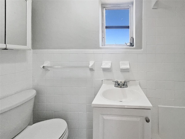 bathroom featuring vanity, tile walls, toilet, and a wainscoted wall