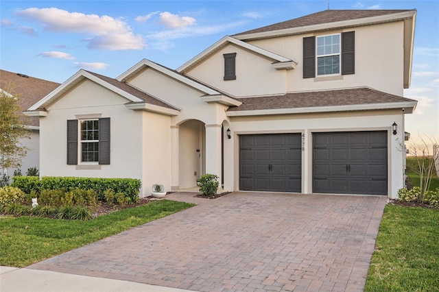 traditional home featuring stucco siding, an attached garage, decorative driveway, and roof with shingles