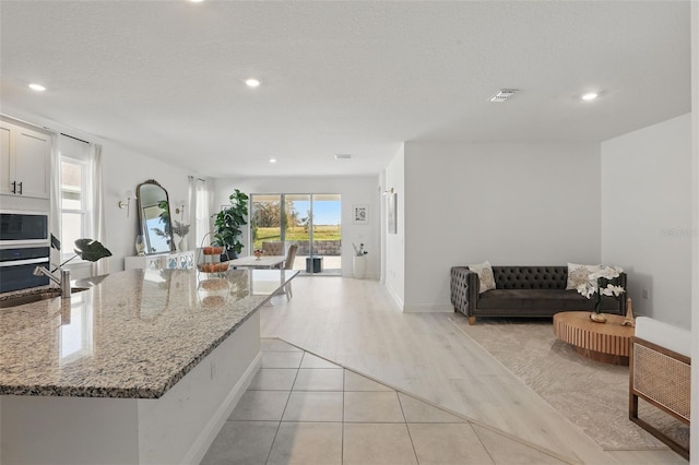 kitchen with visible vents, a sink, light stone counters, open floor plan, and built in microwave