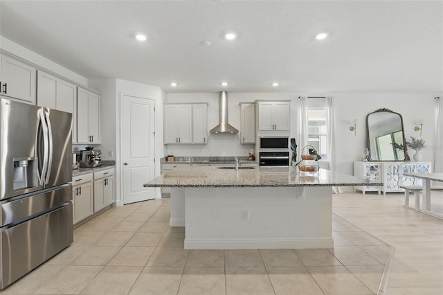 kitchen with oven, built in microwave, stainless steel fridge, wall chimney exhaust hood, and a kitchen island with sink