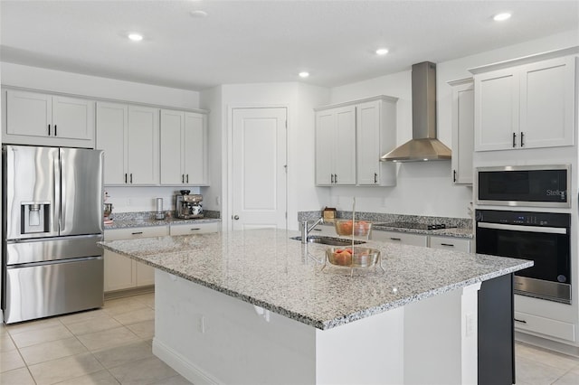 kitchen with recessed lighting, a kitchen island with sink, a sink, appliances with stainless steel finishes, and wall chimney range hood