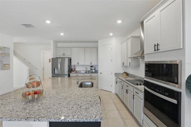 kitchen with visible vents, wall chimney range hood, appliances with stainless steel finishes, a large island, and a sink