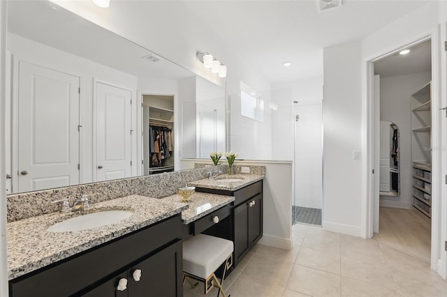 bathroom with a walk in shower, a walk in closet, double vanity, tile patterned floors, and a sink