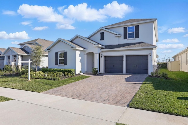 traditional home featuring a front lawn, fence, stucco siding, decorative driveway, and an attached garage