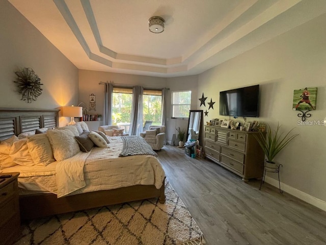 bedroom with a tray ceiling, baseboards, and wood finished floors