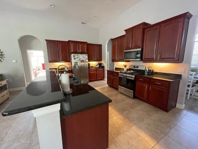 kitchen with dark countertops, a sink, appliances with stainless steel finishes, arched walkways, and reddish brown cabinets