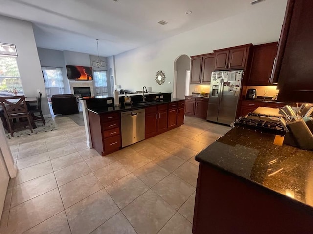 kitchen with a tiled fireplace, a sink, arched walkways, appliances with stainless steel finishes, and light tile patterned flooring