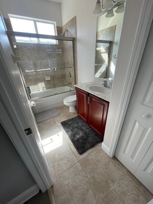 bathroom with combined bath / shower with glass door, toilet, vanity, and tile patterned flooring