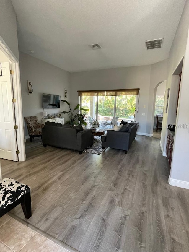 living room featuring wood finished floors, visible vents, arched walkways, and baseboards