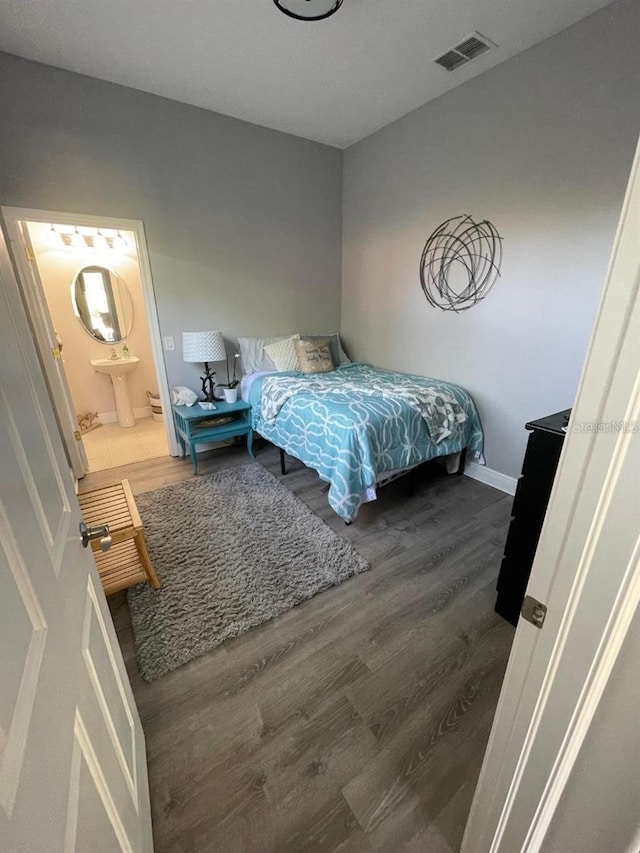 bedroom featuring visible vents, ensuite bath, baseboards, and wood finished floors