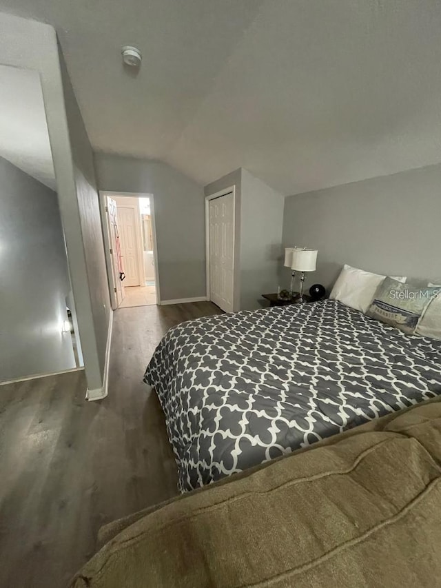 bedroom with a closet, vaulted ceiling, baseboards, and wood finished floors