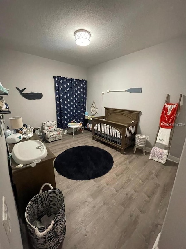 bedroom featuring a nursery area, a textured ceiling, and wood finished floors