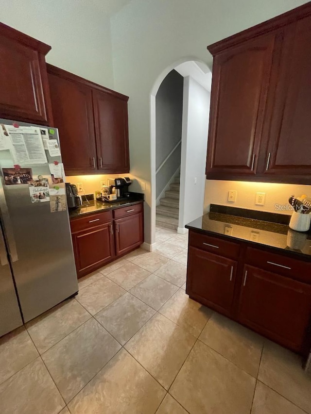 kitchen featuring dark brown cabinets, baseboards, light tile patterned floors, freestanding refrigerator, and arched walkways