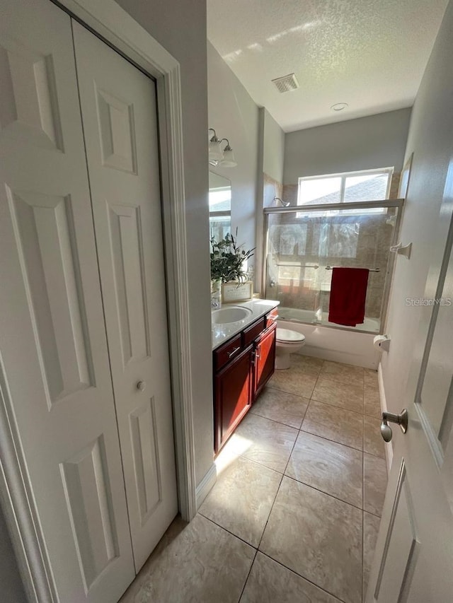 full bathroom featuring vanity, shower / bath combination with glass door, tile patterned flooring, a textured ceiling, and toilet