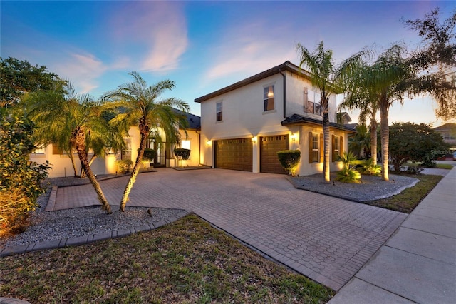 view of front of home with decorative driveway, an attached garage, and stucco siding