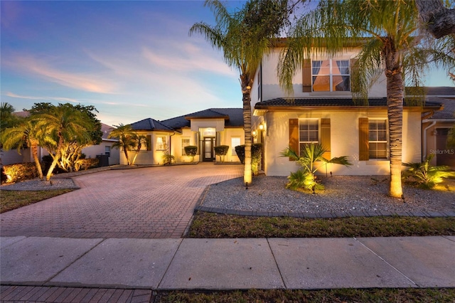 view of front facade with stucco siding, a tile roof, and decorative driveway