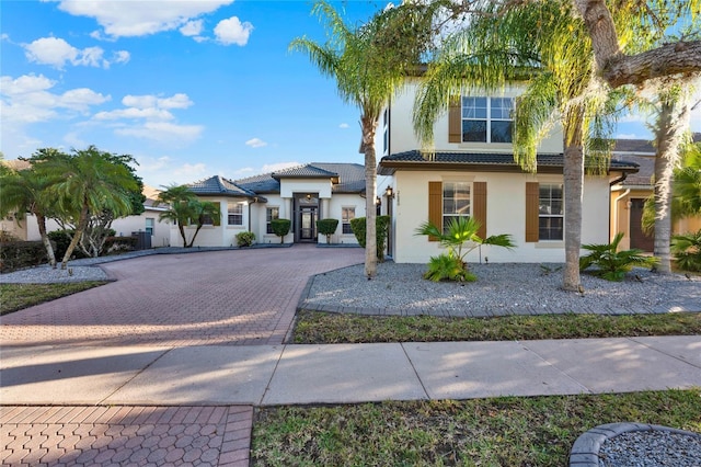 view of front of property featuring a tiled roof, decorative driveway, and stucco siding