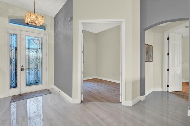 foyer with arched walkways, tile patterned floors, baseboards, and an inviting chandelier