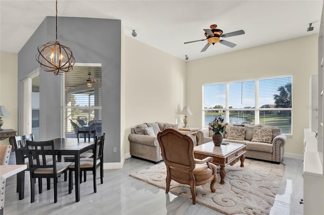 living area featuring plenty of natural light, ceiling fan with notable chandelier, and baseboards