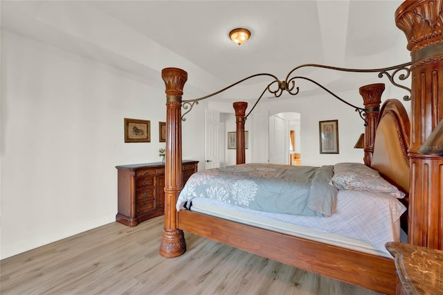 bedroom with light wood finished floors, arched walkways, and baseboards