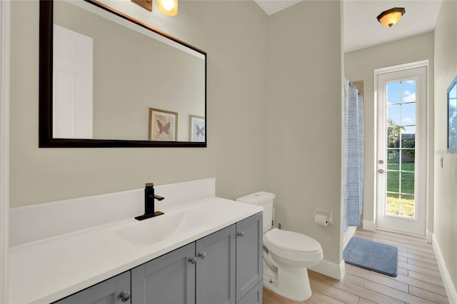 bathroom with baseboards, toilet, a shower with shower curtain, wood finished floors, and vanity