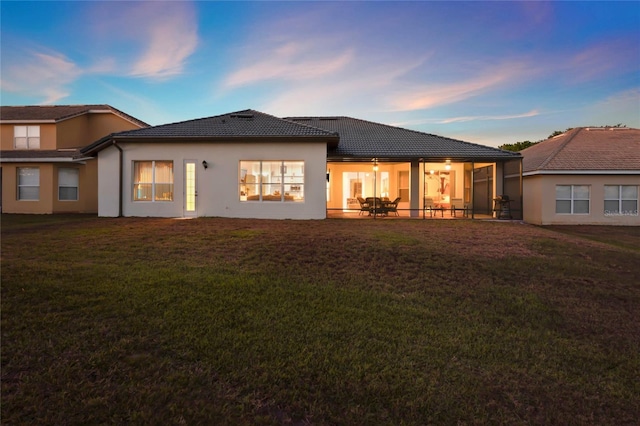 back of property at dusk with a tile roof, a yard, a patio area, and stucco siding