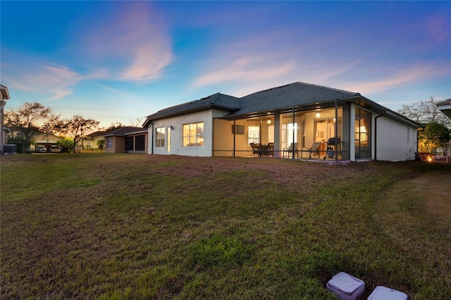 back of house at dusk with a patio, cooling unit, stucco siding, a tiled roof, and a lawn