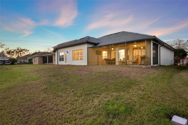 back of property with stucco siding, a lawn, a tiled roof, and a sunroom