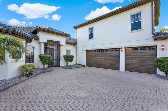 view of front of house with a tiled roof, decorative driveway, an attached garage, and stucco siding