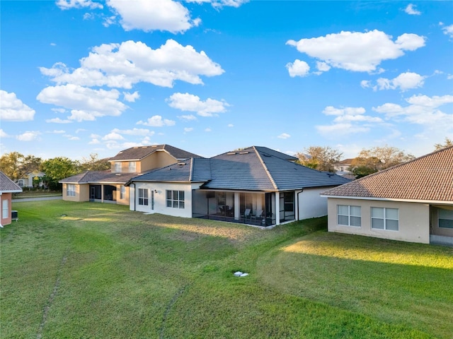 back of house with a tile roof, a lawn, a sunroom, and stucco siding