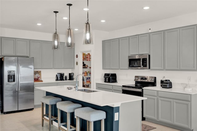 kitchen featuring an island with sink, recessed lighting, gray cabinets, a sink, and stainless steel appliances