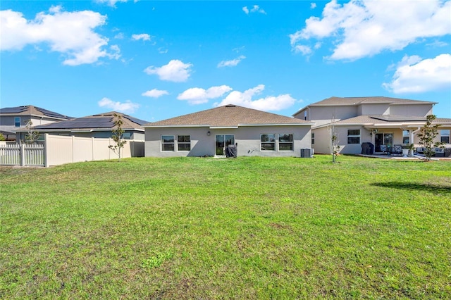 rear view of house with stucco siding, a lawn, cooling unit, and fence