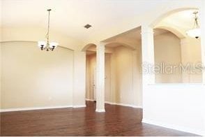 spare room featuring baseboards, arched walkways, an inviting chandelier, and wood finished floors