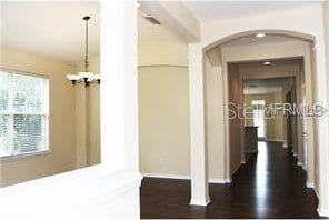 hall with baseboards, arched walkways, a notable chandelier, and dark wood-style floors