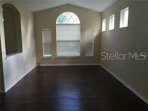 unfurnished room featuring baseboards, lofted ceiling, arched walkways, and wood finished floors