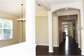 corridor with arched walkways, a notable chandelier, and dark wood-style flooring