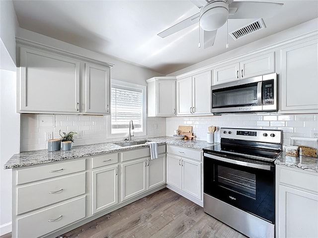 kitchen featuring visible vents, a sink, tasteful backsplash, appliances with stainless steel finishes, and light wood finished floors