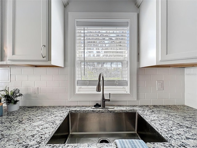 kitchen with a sink, light stone countertops, and tasteful backsplash