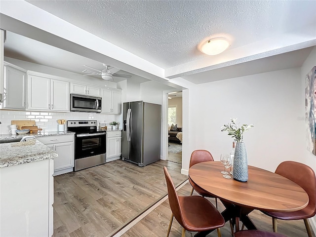 kitchen with light wood-type flooring, tasteful backsplash, a textured ceiling, appliances with stainless steel finishes, and white cabinets