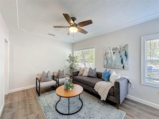 living room featuring light wood finished floors, visible vents, a healthy amount of sunlight, and ceiling fan