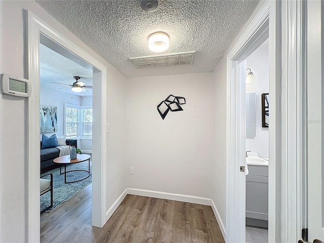 corridor featuring baseboards, wood finished floors, visible vents, and a textured ceiling