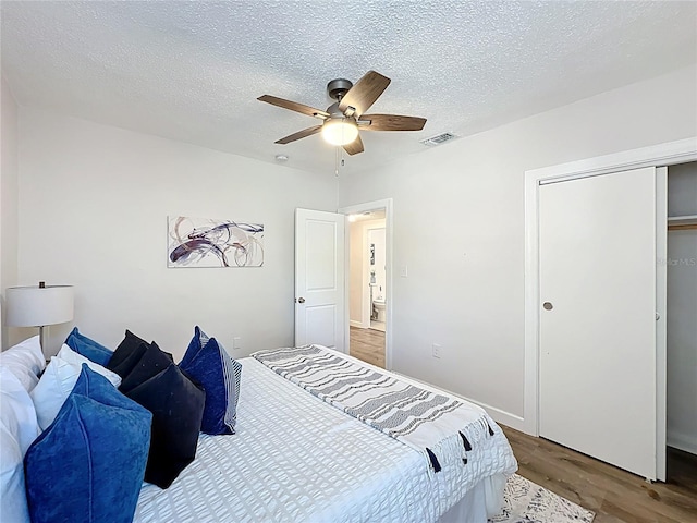 bedroom with visible vents, a ceiling fan, a textured ceiling, wood finished floors, and a closet