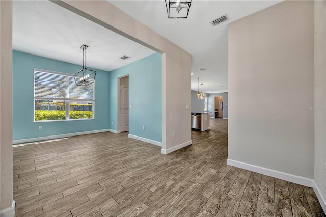 unfurnished room featuring visible vents, baseboards, a notable chandelier, and wood finished floors