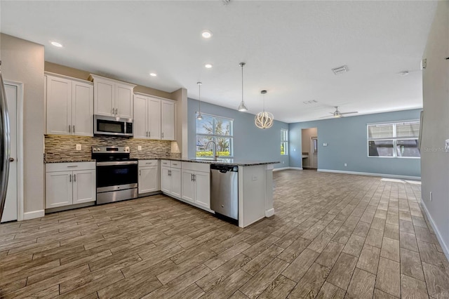 kitchen with stainless steel appliances, backsplash, a peninsula, and white cabinetry